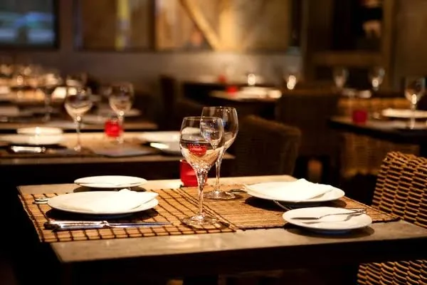 Table for two laid with white plates, folded napkins and wine glasses in a softly lit dining room